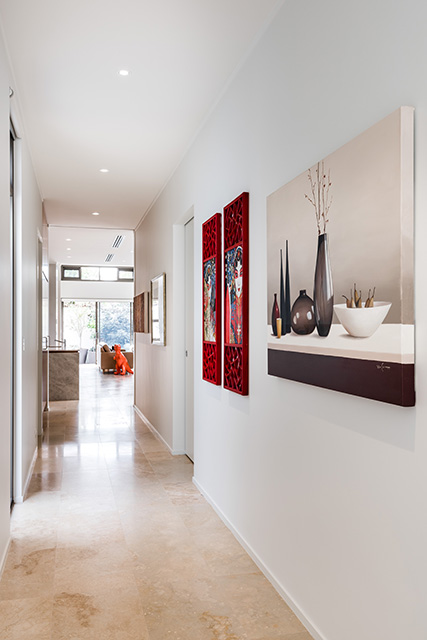 Bright hallway with beige stone flooring, white walls, red decorative panels, and framed artwork leading to a living area