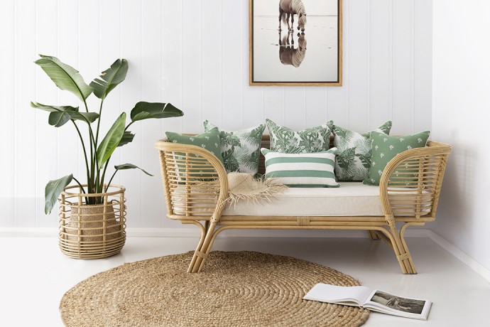 Cozy living room corner with rattan daybed, green patterned pillows, potted plant, and woven rug, soft neutral and green